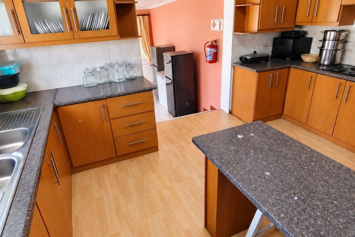 A functional kitchen featuring wood-look cabinetry, laminate countertops, a central island, and a double stainless steel sink with tiled backsplash.