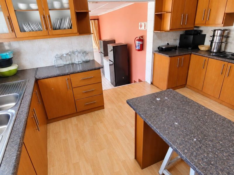 A functional kitchen featuring wood-look cabinetry, laminate countertops, a central island, and a double stainless steel sink with tiled backsplash.