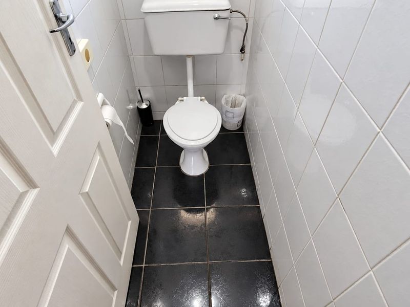 A compact, functional bathroom featuring white wall tiles, dark floor tiles, and a standard toilet suite.