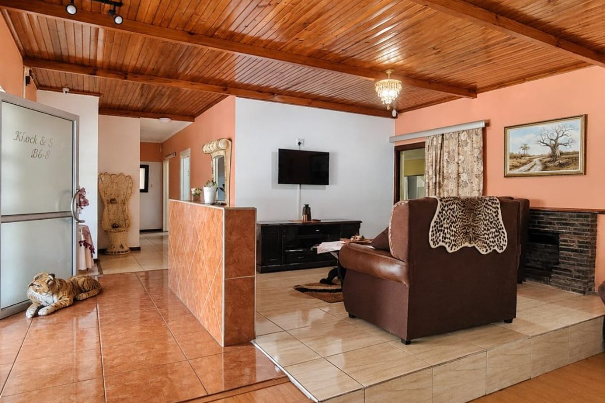 Spacious living area featuring a timber-clad ceiling, split-level tiled flooring, and a built-in brick fireplace, offering a warm and rustic aesthetic.