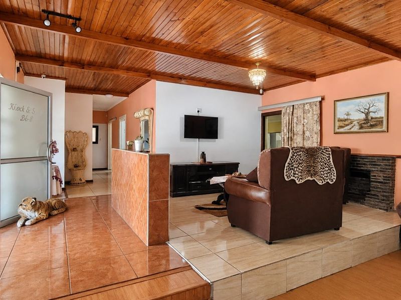Spacious living area featuring a timber-clad ceiling, split-level tiled flooring, and a built-in brick fireplace, offering a warm and rustic aesthetic.