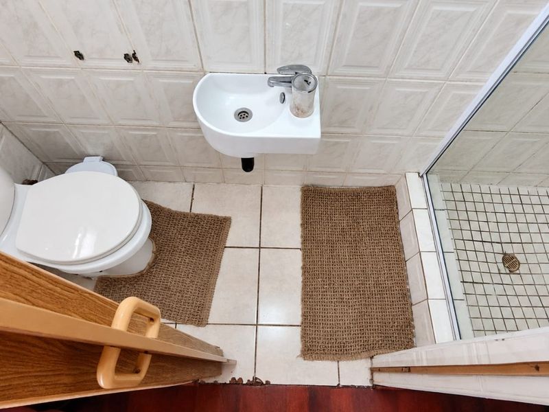 Compact bathroom featuring a wall-mounted basin, toilet, and shower enclosure with tiled finishes. The space shows signs of wear and requires maintenance.