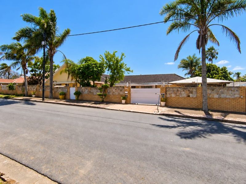 Front street view of the property featuring a secure brick and stone boundary wall, sliding gate, and established palm trees.