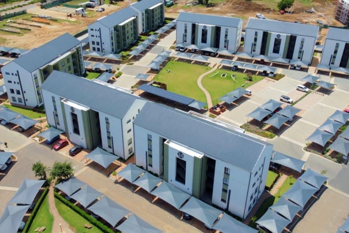 Aerial view of a modern apartment complex featuring multiple residential blocks, landscaped communal green spaces, and extensive covered parking facilities.
