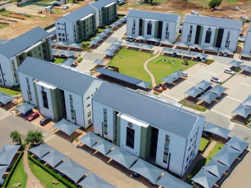 Aerial view of a modern apartment complex featuring multiple residential blocks, landscaped communal green spaces, and extensive covered parking facilities.