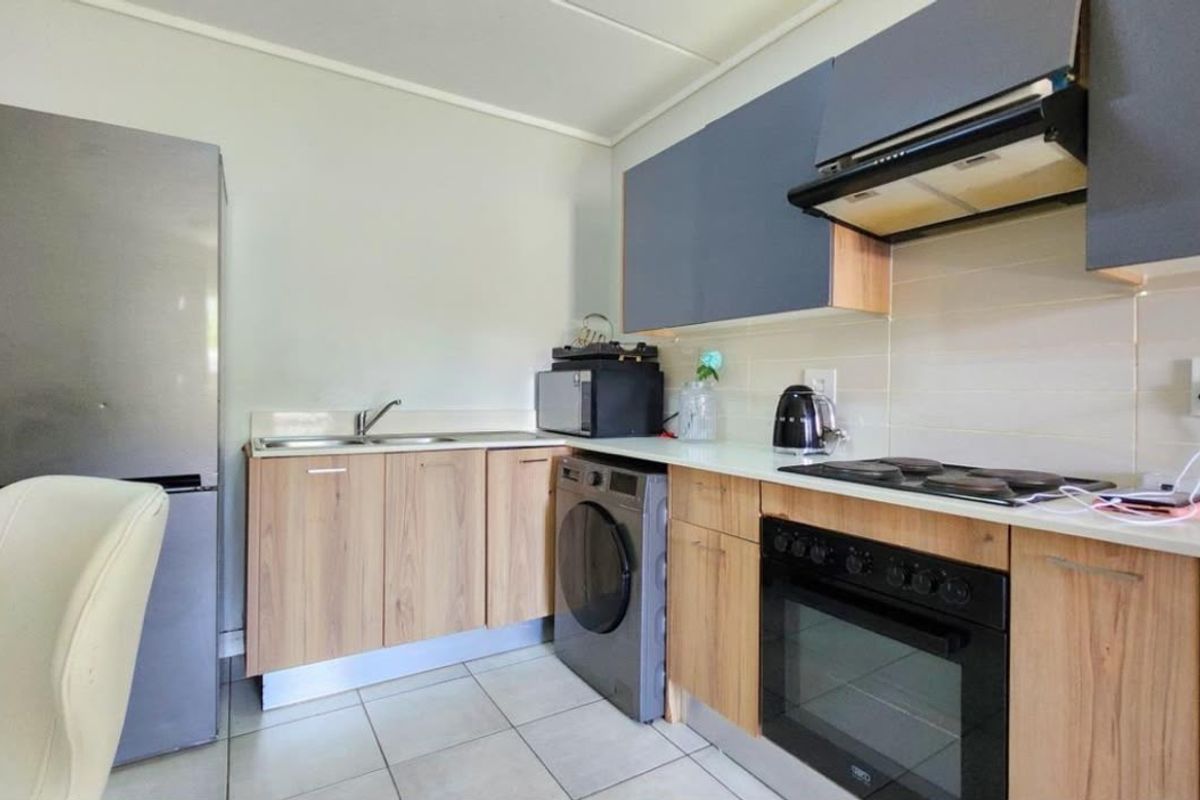 A functional kitchen featuring wood-finish cabinetry, a built-in oven with hob, extractor fan, and tiled flooring, providing a practical workspace.