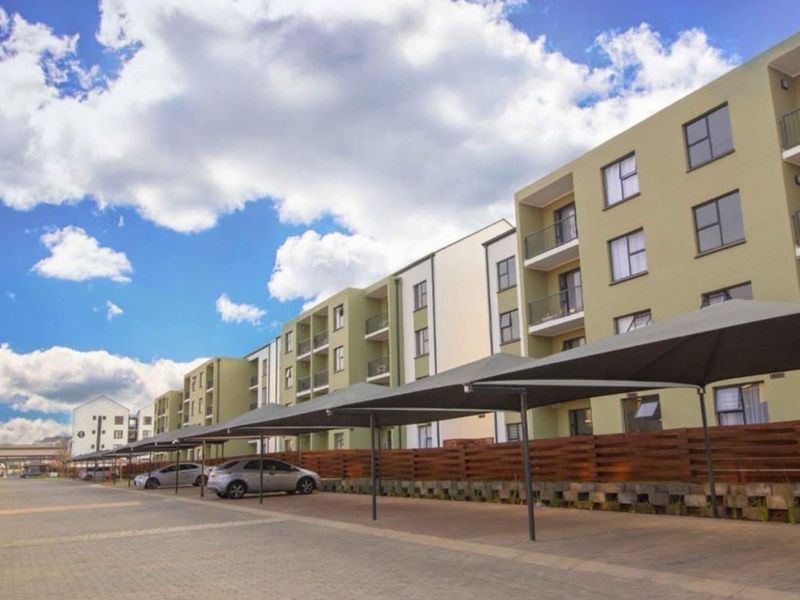 Exterior view of a modern apartment complex featuring paved parking areas with shade cloth carports and private balconies.