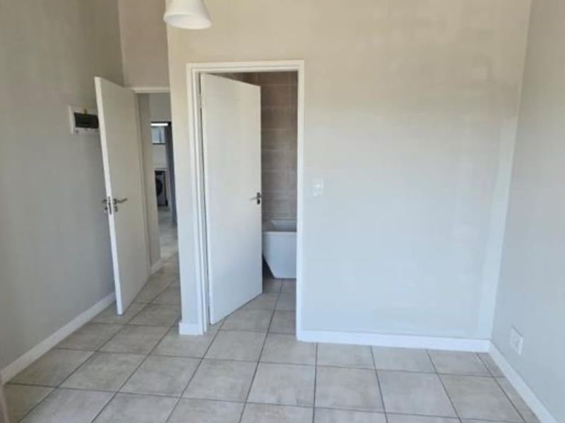 A clean, empty hallway featuring neutral tiled flooring, white internal doors, and access to an adjacent bathroom and utility area.