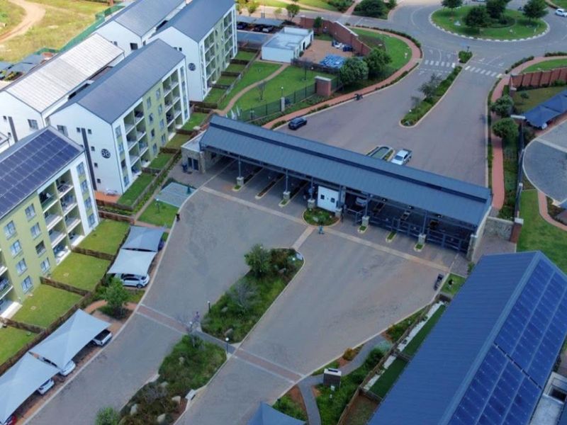 Aerial view of a modern residential apartment complex featuring solar-equipped buildings, a secure gated entrance, and dedicated covered parking areas.