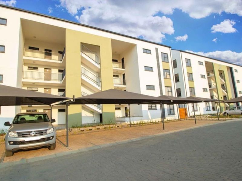 Modern apartment complex exterior featuring paved parking areas with shade cloth carports and multi-level residential units with balconies.