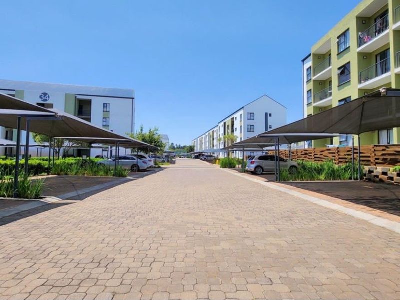 A well-maintained apartment complex featuring paved driveways, covered parking bays, and multi-story residential buildings with balconies.