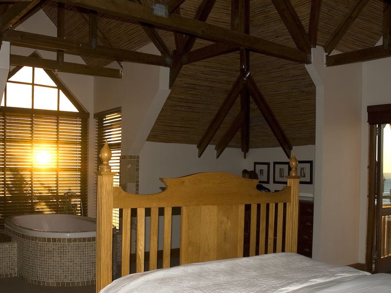Spacious bedroom featuring exposed timber trusses, a thatched ceiling, an integrated bathtub, and direct access to a balcony with ocean views.