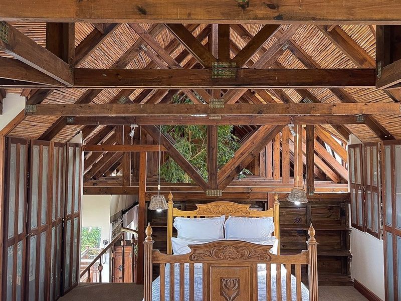 A unique bedroom featuring high vaulted ceilings with exposed timber trusses, built-in wooden cabinetry, and integrated timber shutters.