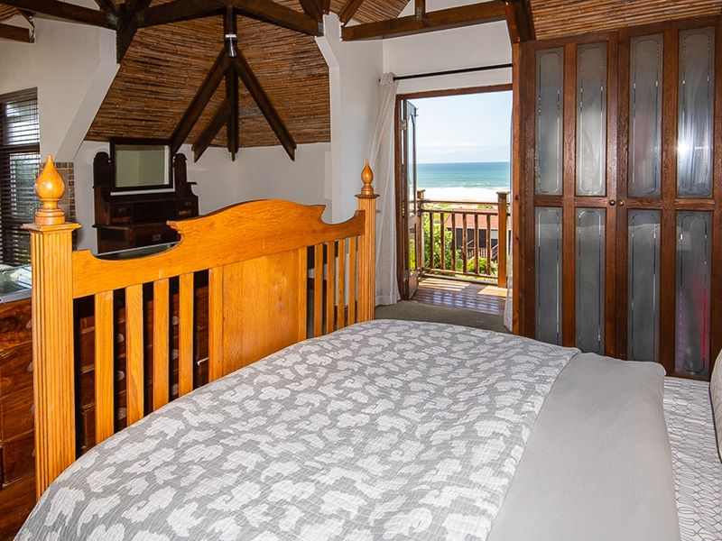 Spacious bedroom featuring exposed timber roof trusses, thatched ceiling, built-in wooden cabinetry, and direct access to a private balcony with ocean views.