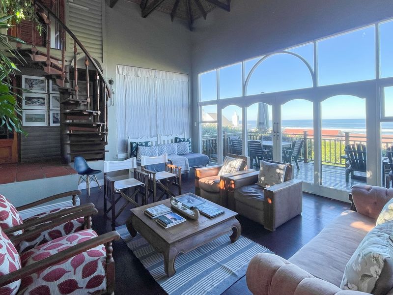 Spacious living room featuring a striking spiral staircase, vaulted ceilings, and expansive glass doors opening onto a scenic ocean-view deck.