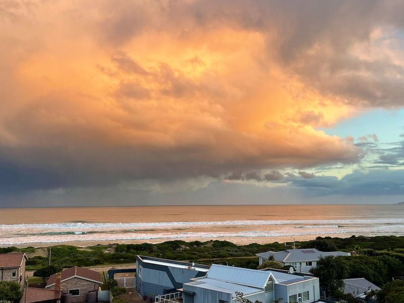 A scenic elevated view overlooking the coastline, beach, and surrounding residential neighborhood under a dramatic sunset sky.