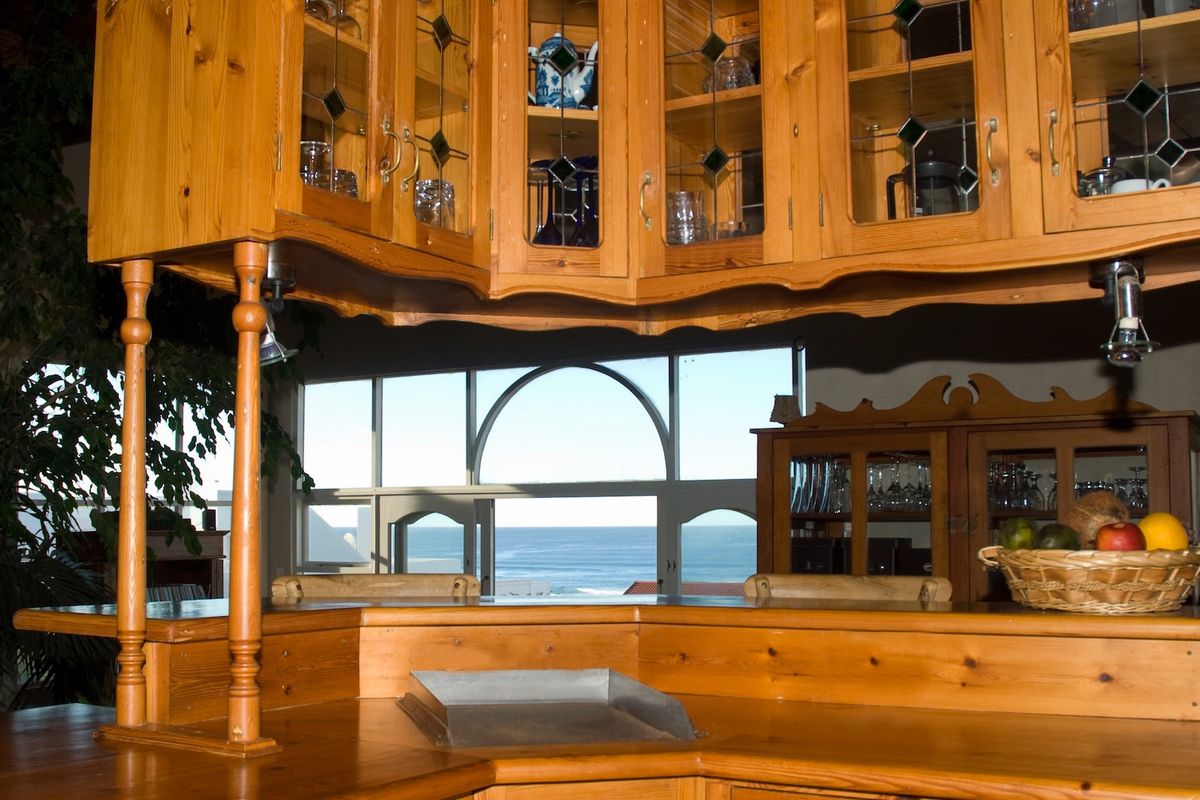 A kitchen area featuring extensive wooden cabinetry and a breakfast bar, offering a scenic view of the ocean through large windows.