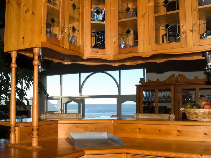 A kitchen area featuring extensive wooden cabinetry and a breakfast bar, offering a scenic view of the ocean through large windows.
