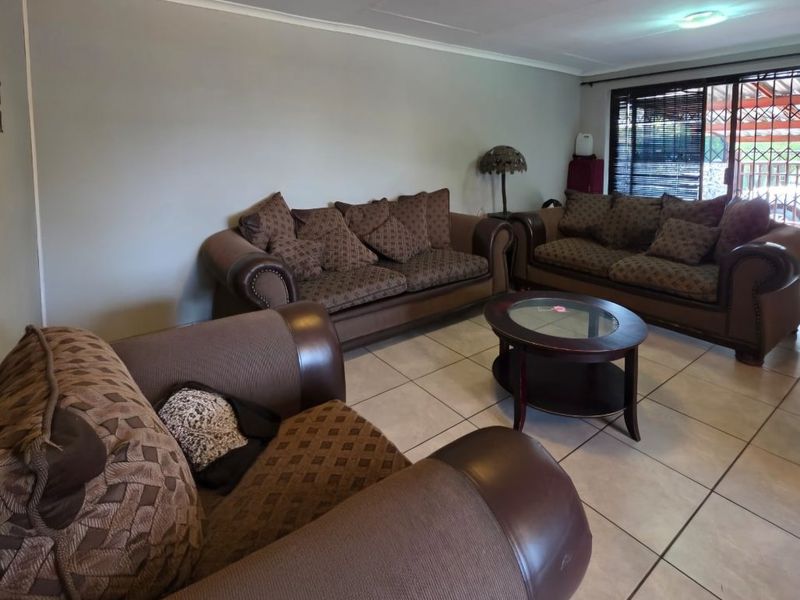 A spacious living room featuring neutral wall tones, ceramic floor tiles, and a sliding glass door providing access to the outdoor area.