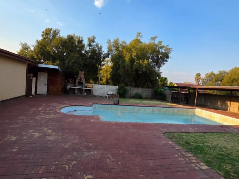 Outdoor pool area featuring a swimming pool, brick paved patio, and a built-in braai, set within a private backyard with boundary walls.