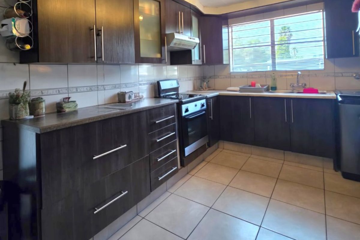 A functional kitchen featuring dark wood cabinetry, tiled flooring, a built-in oven with extractor fan, and ample counter space with a tiled backsplash.