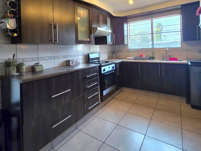 A functional kitchen featuring dark wood cabinetry, tiled flooring, a built-in oven with extractor fan, and ample counter space with a tiled backsplash.