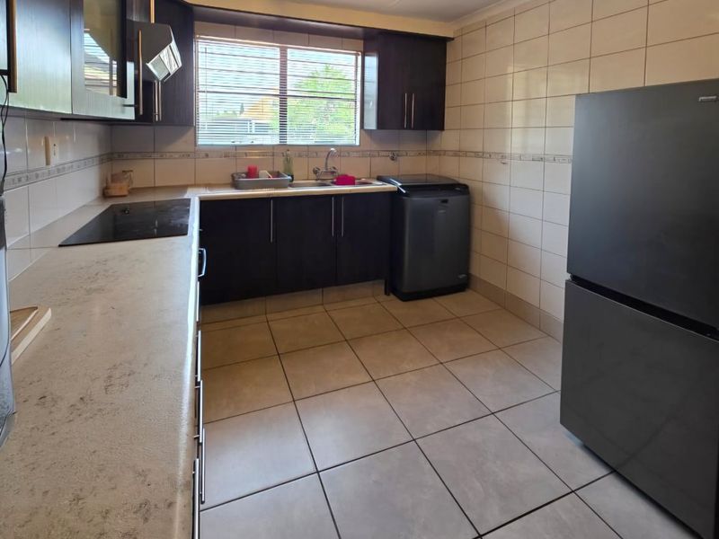 A functional kitchen featuring dark cabinetry, light laminate countertops, ceramic wall and floor tiling, and integrated cooking appliances.