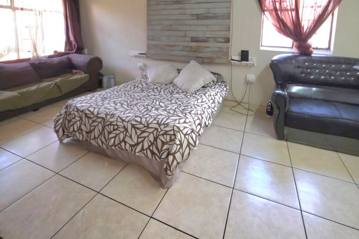 A spacious bedroom featuring tiled flooring, a ceiling fan, and decorative wall paneling, offering a functional layout with ample natural light.