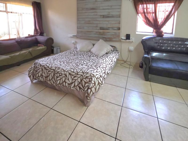 A spacious bedroom featuring tiled flooring, a ceiling fan, and decorative wall paneling, offering a functional layout with ample natural light.