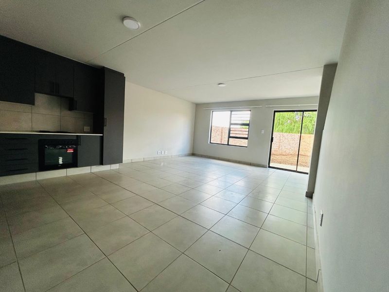 An open-plan living and kitchen area featuring modern dark cabinetry, tiled flooring, and direct access to the rear outdoor space through a sliding door.