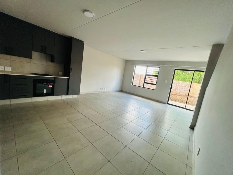 Spacious open-plan living area featuring modern dark cabinetry, built-in oven and hob, tiled flooring, and direct access to the rear garden via sliding doors.