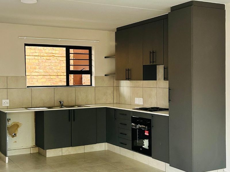 Modern kitchen featuring dark grey cabinetry, built-in oven, electric hob, and tiled backsplash. The space is currently vacant and ready for final finishing touches.