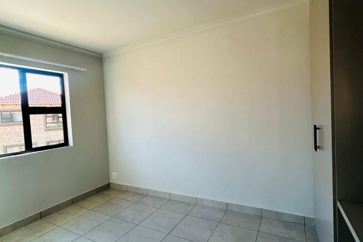 A clean, empty bedroom featuring neutral tiled flooring, built-in cupboards, and a large window providing natural light.