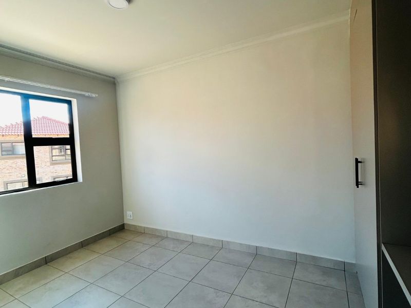 A clean, empty bedroom featuring neutral tiled flooring, built-in cupboards, and a large window providing natural light.