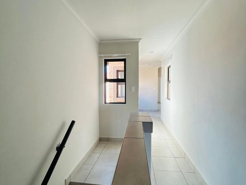 A bright, tiled hallway featuring a staircase with a metal handrail and a tiled balustrade, leading to an open landing area.