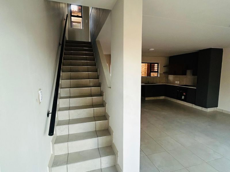 Open plan living area featuring a tiled staircase with a modern handrail, leading to a kitchen with dark built-in cabinetry and tiled flooring.