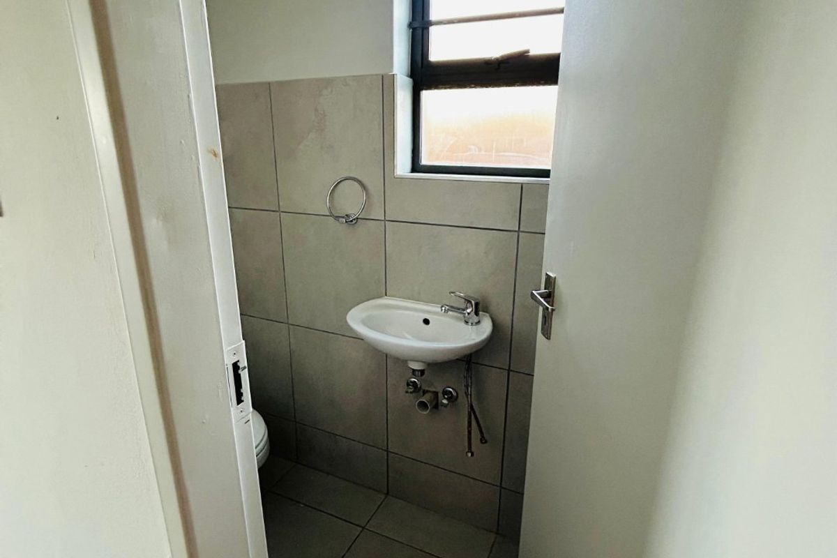 A compact guest bathroom featuring a wall-mounted basin, tiled flooring, and a louvered window for ventilation.