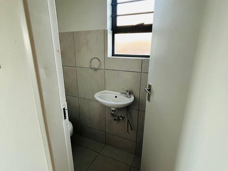 A compact guest bathroom featuring a wall-mounted basin, tiled flooring, and a louvered window for ventilation.