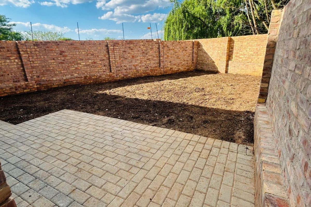 A private rear courtyard featuring a paved patio area and a large open garden space enclosed by high brick boundary walls.