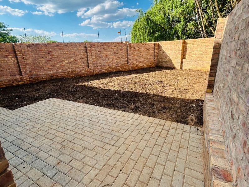 A private rear courtyard featuring a paved patio area and a large open garden space enclosed by high brick boundary walls.