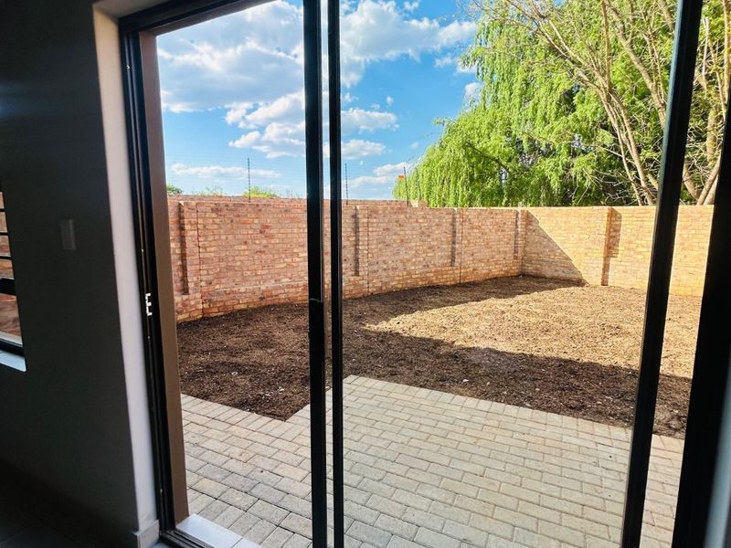 View from an interior living space through a sliding glass door onto a paved patio and private garden area with brick boundary walls.