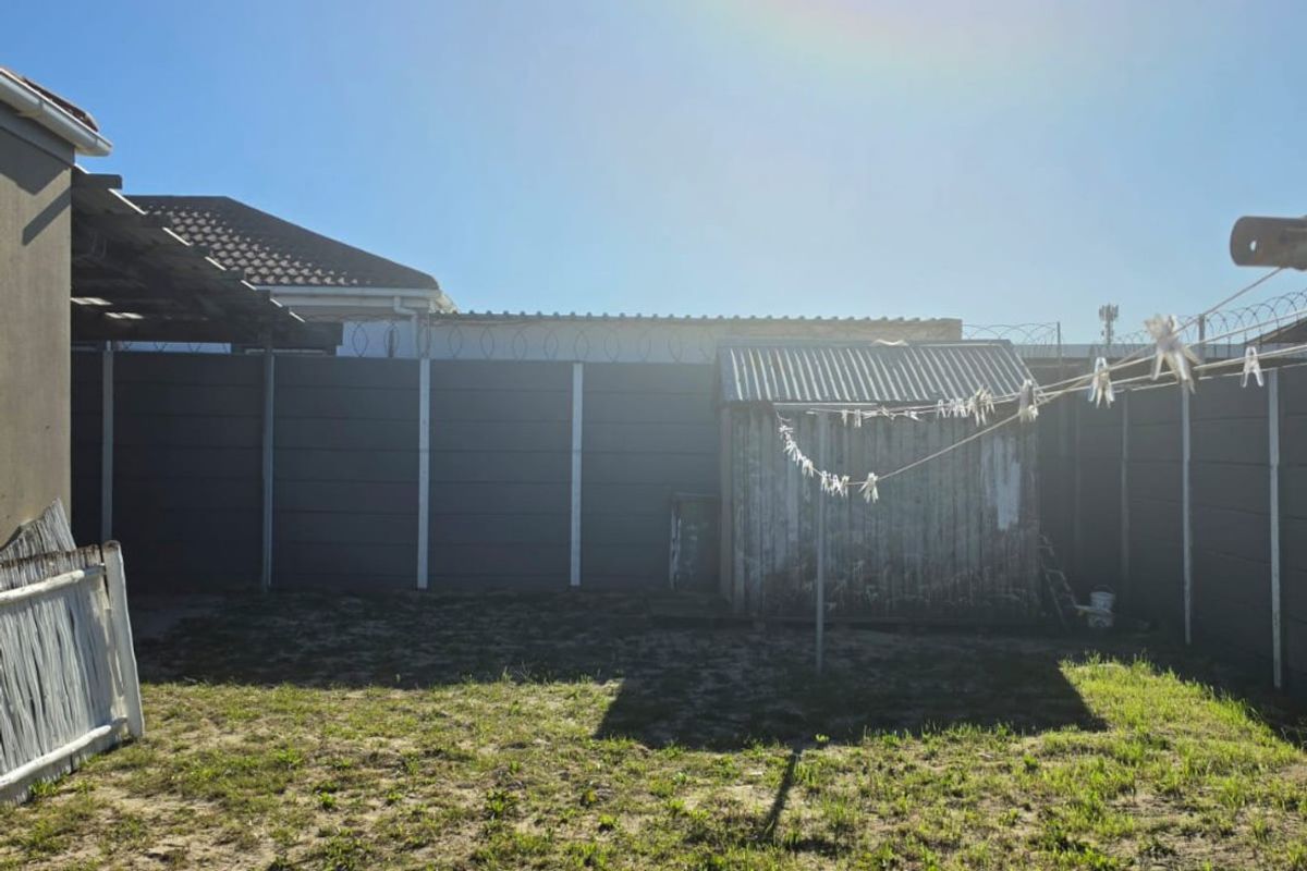 Rear garden area featuring a precast concrete boundary wall with security razor wire and a weathered corrugated metal storage shed.