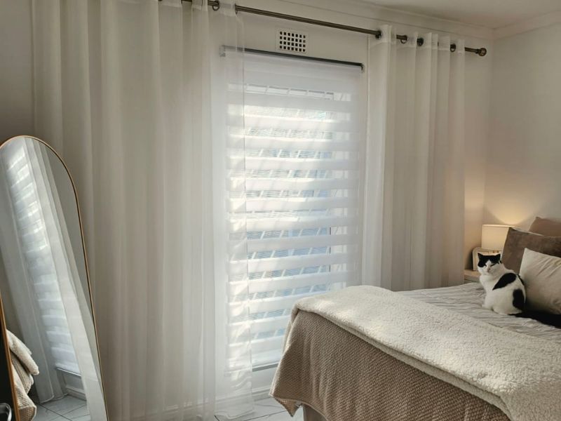 A bright and well-maintained bedroom featuring tiled flooring, a ventilation grille, and floor-to-ceiling curtains.