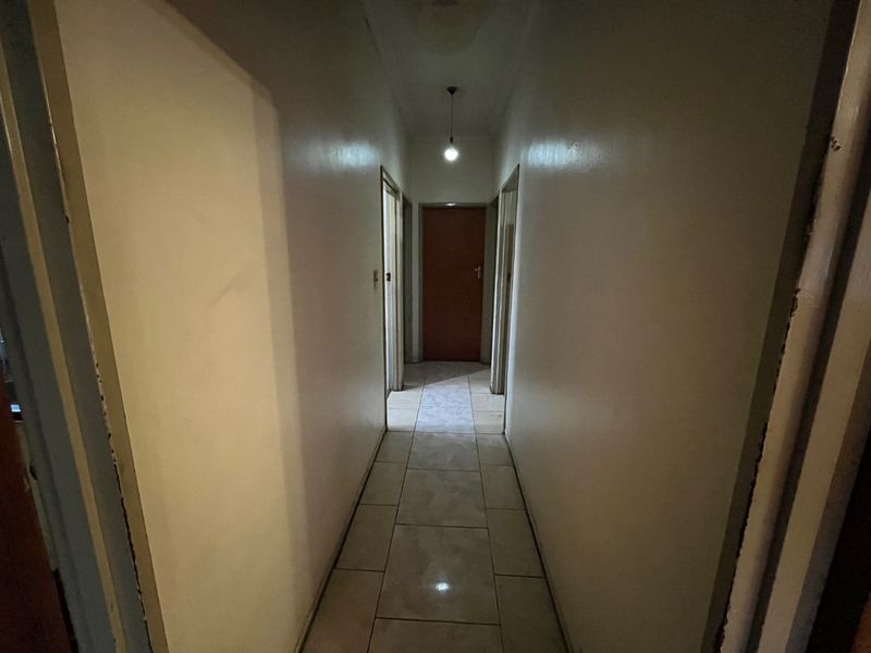A narrow residential hallway featuring tiled flooring and a central pendant light fixture, providing access to multiple rooms.