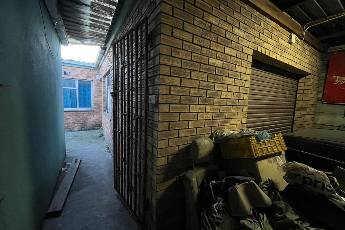A narrow exterior passage featuring brick walls, a security gate, and a roller shutter door leading to a rear paved area.