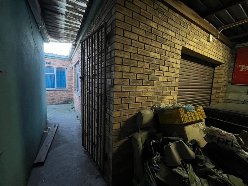 A narrow exterior passage featuring brick walls, a security gate, and a roller shutter door leading to a rear paved area.
