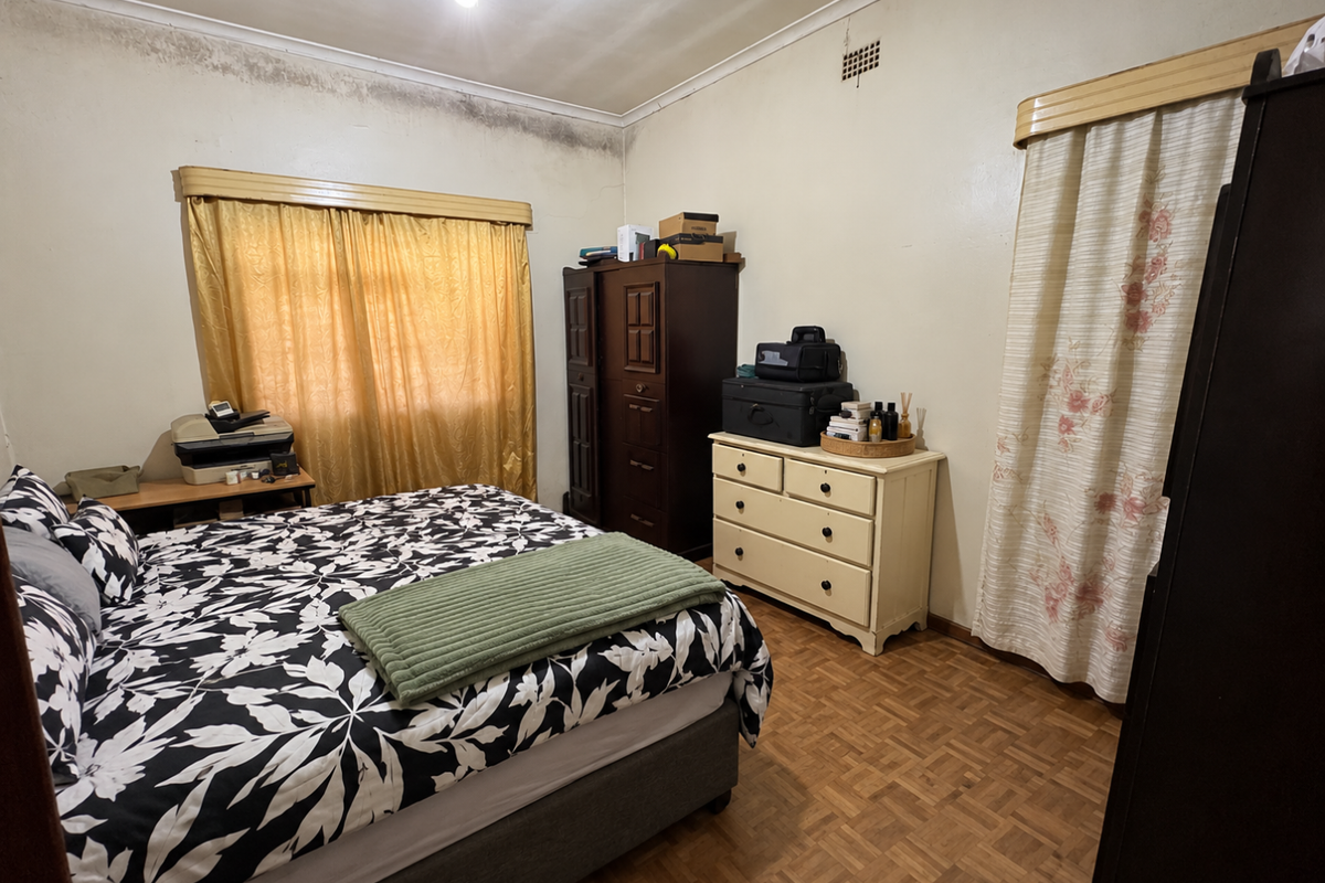 A bedroom featuring parquet flooring and a ceiling fan, currently showing significant signs of damp and wall deterioration requiring maintenance.