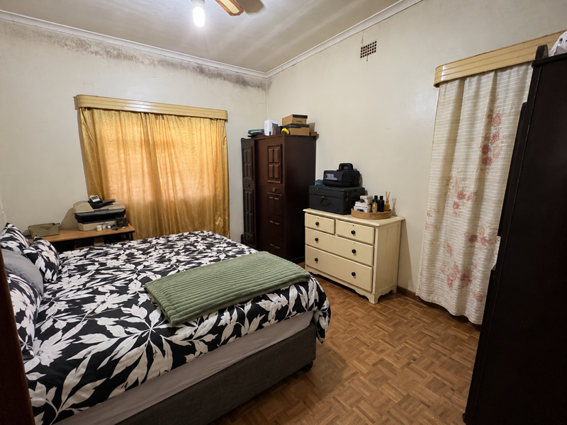 A bedroom featuring parquet flooring and a ceiling fan, currently showing significant signs of damp and wall deterioration requiring maintenance.