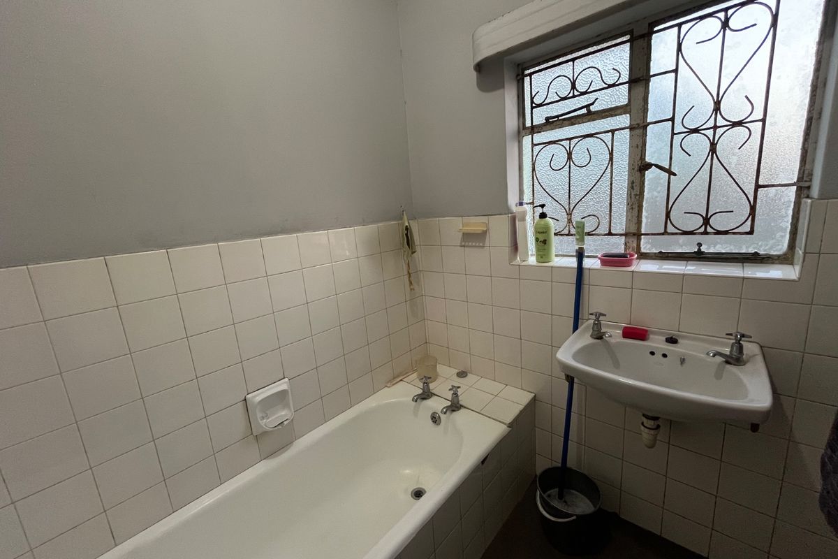 A functional bathroom featuring a standard bathtub, wall-mounted basin, and tiled splashbacks, requiring cosmetic updates to modernize the space.