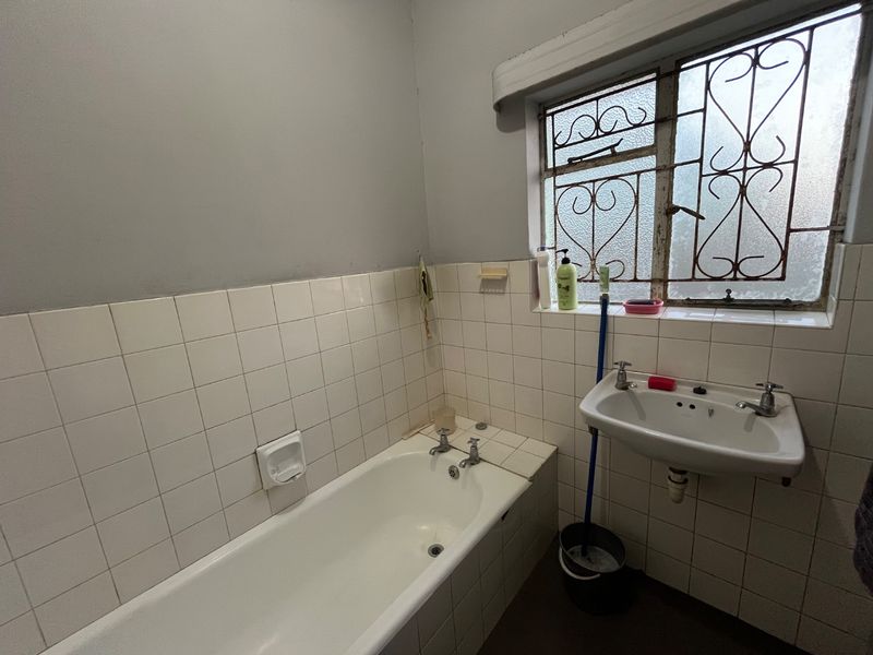 A functional bathroom featuring a standard bathtub, wall-mounted basin, and tiled splashbacks, requiring cosmetic updates to modernize the space.